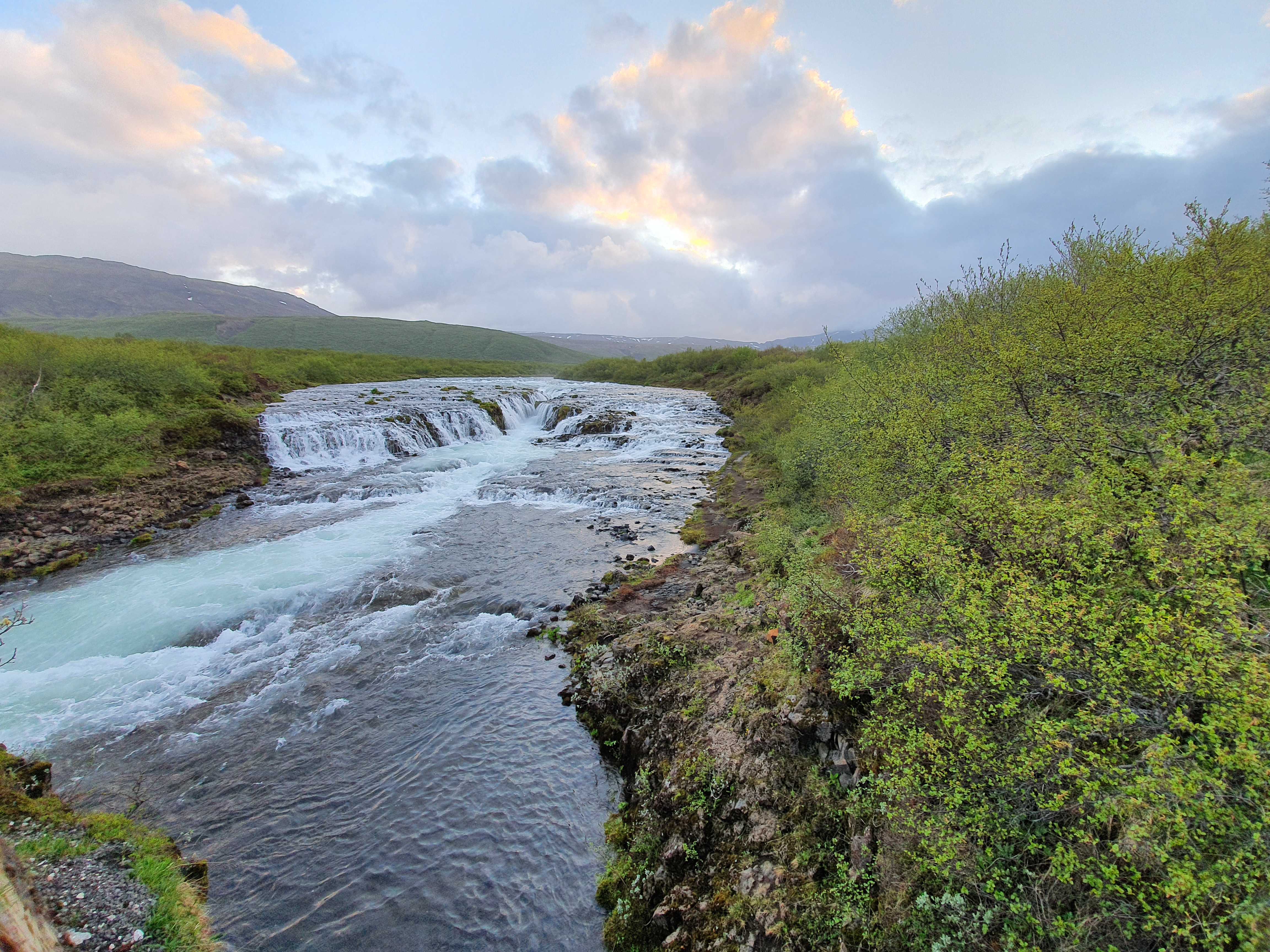 Brúarfoss waterfall with turquoise blue water flowing through lava rock under a dramatic evening sky