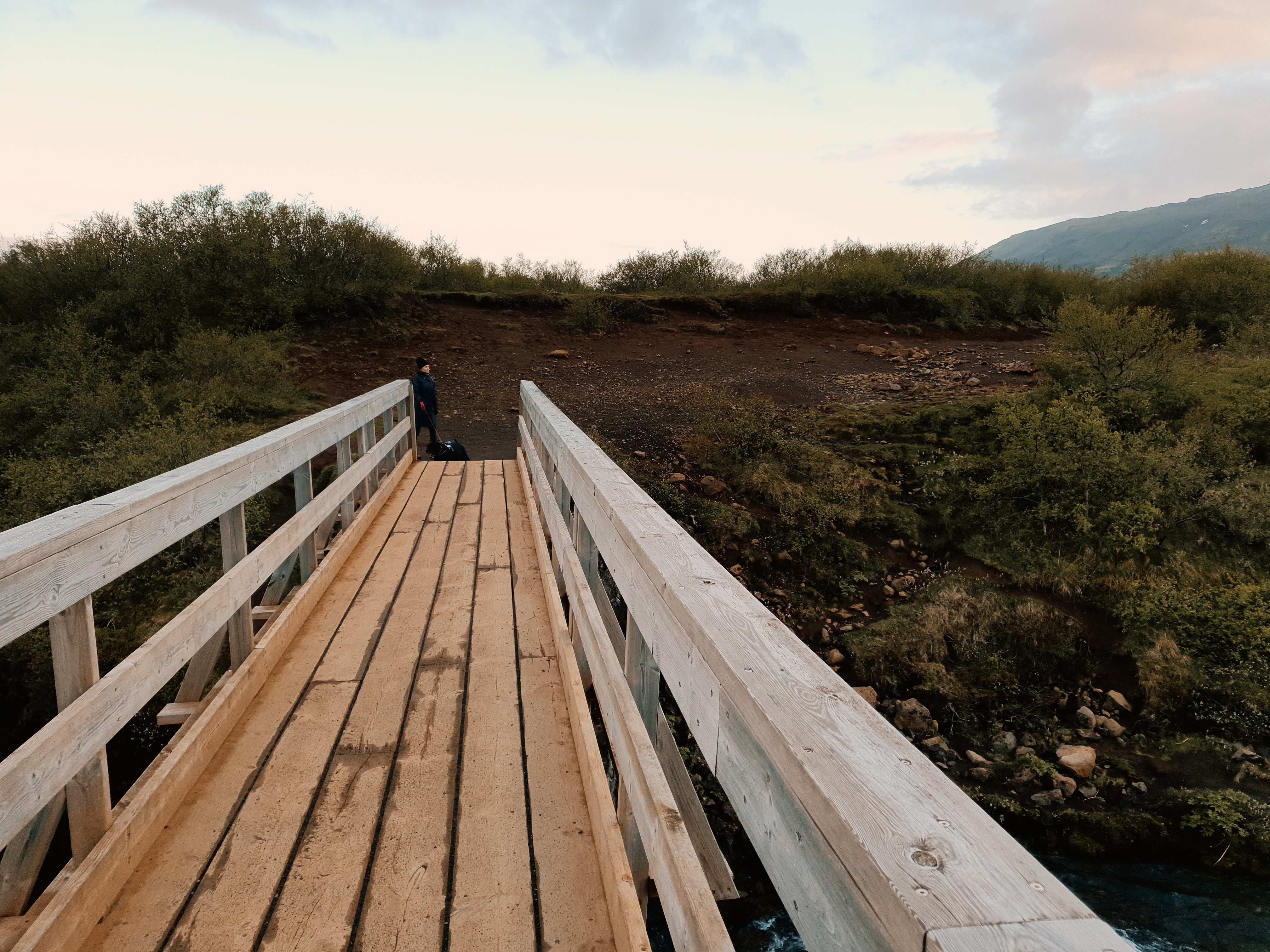 Person crossing the wooden footbridge over the Brúará river near the waterfall