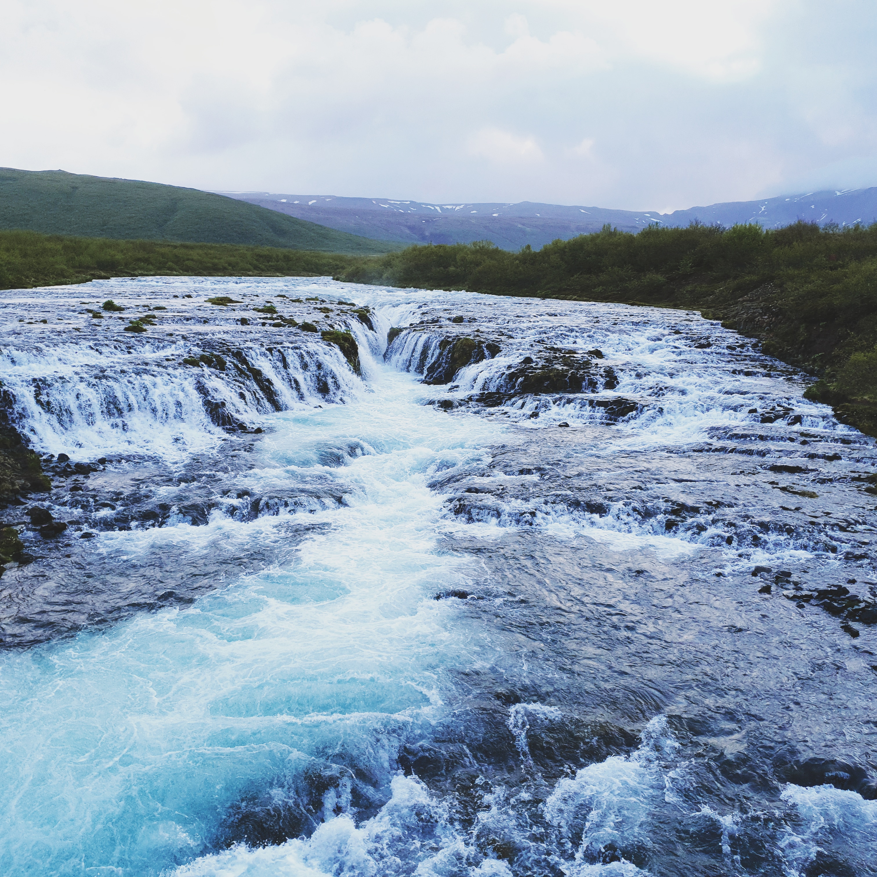 Turquoise blue water of Brúarfoss waterfall flowing through lava rock