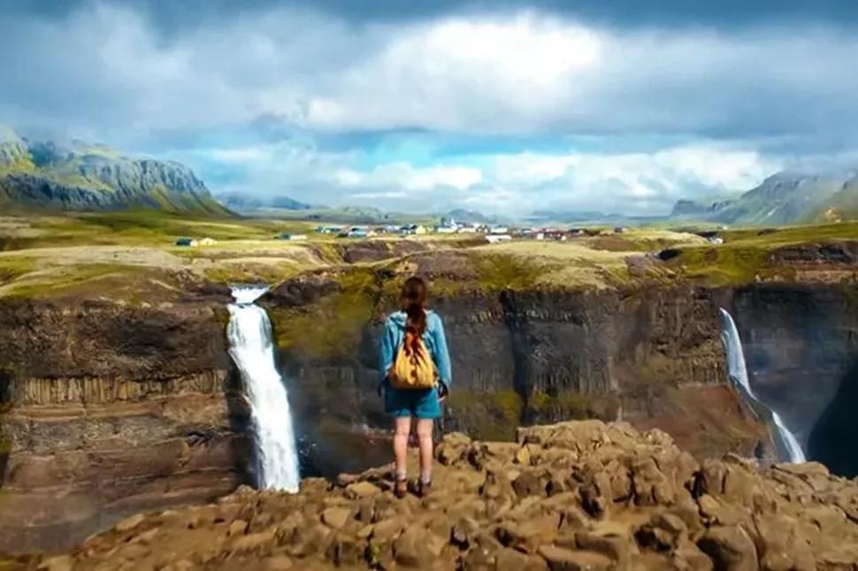 Hiker standing at the edge of Háifoss canyon overlooking both waterfalls with highland landscape beyond