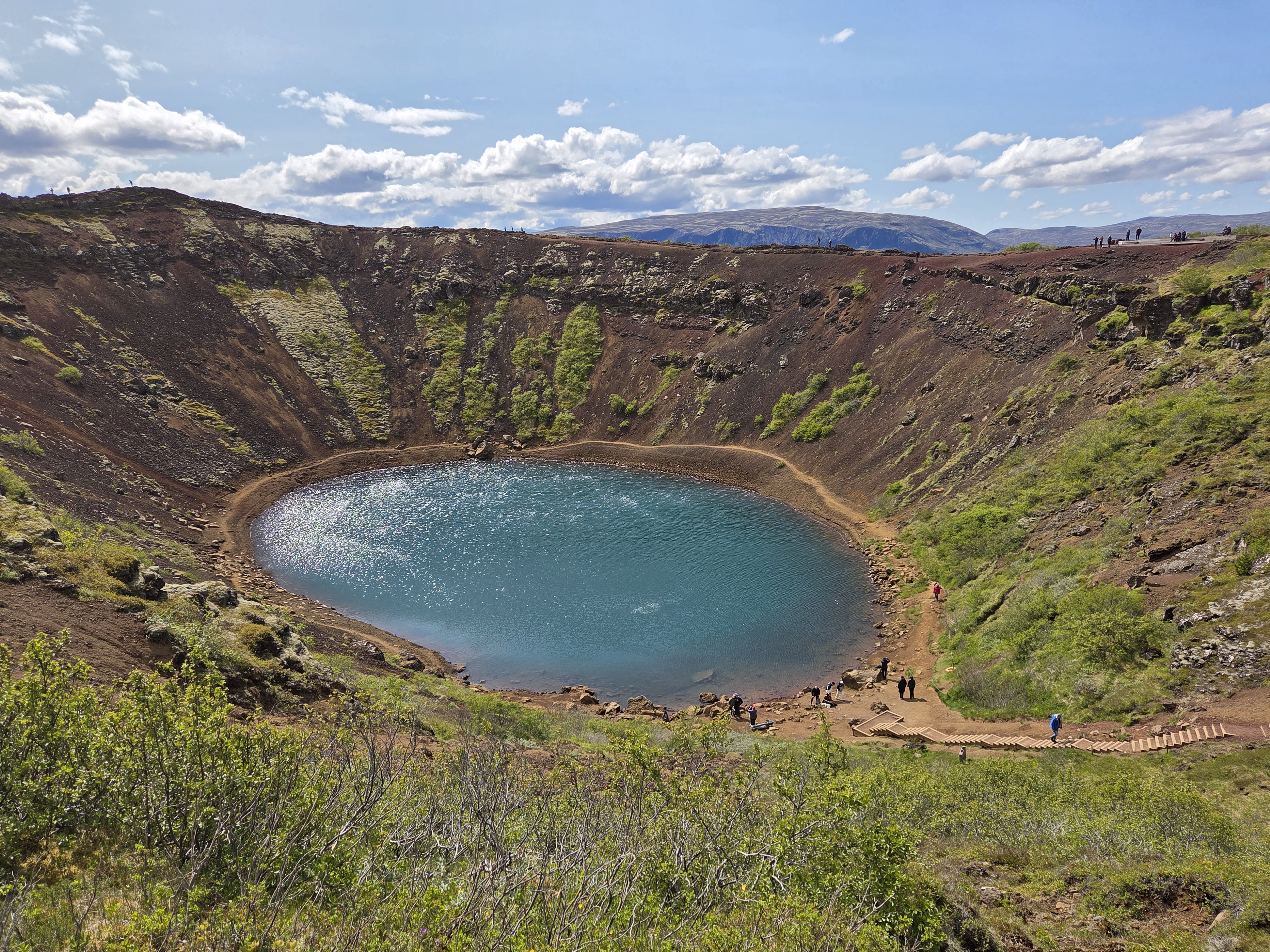 Kerið crater lake with visitors walking down the path to the water's edge