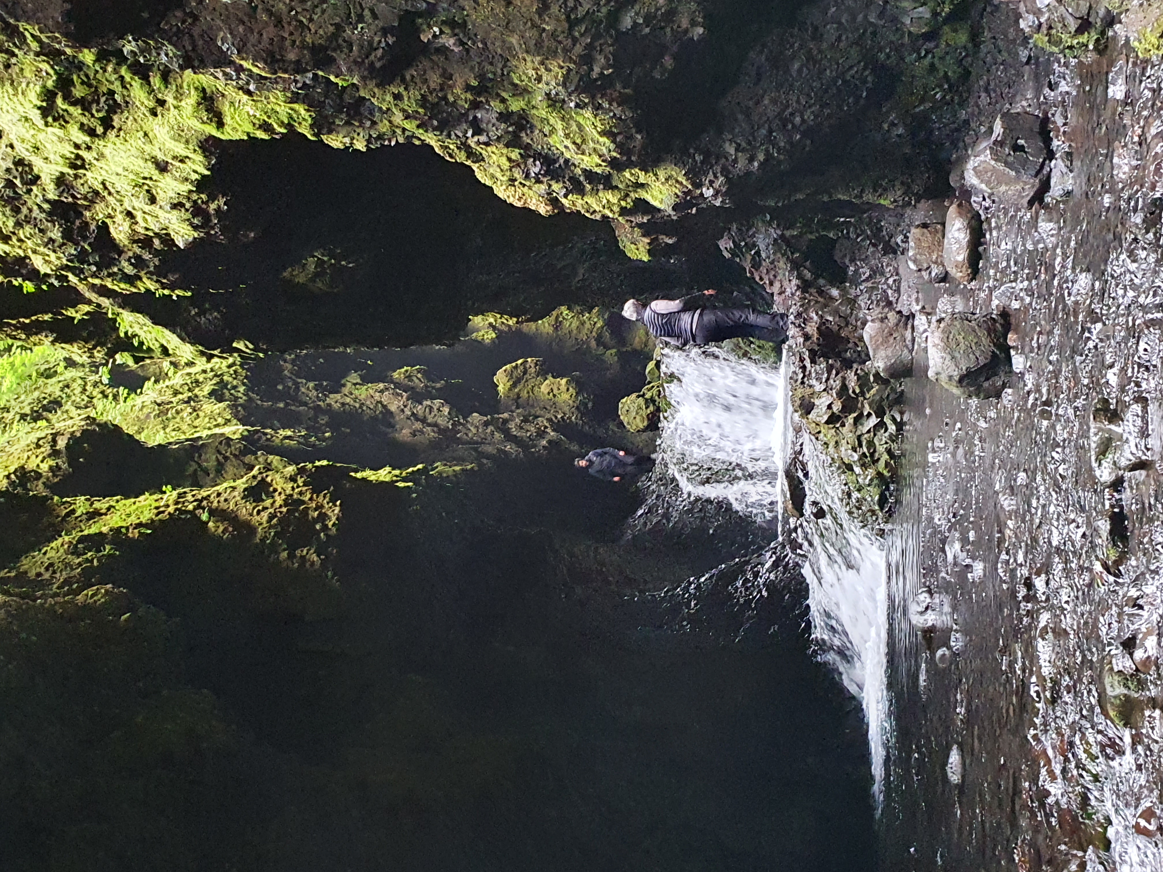 Person navigating near a waterfall inside the dark Nauthúsagil ravine using chains