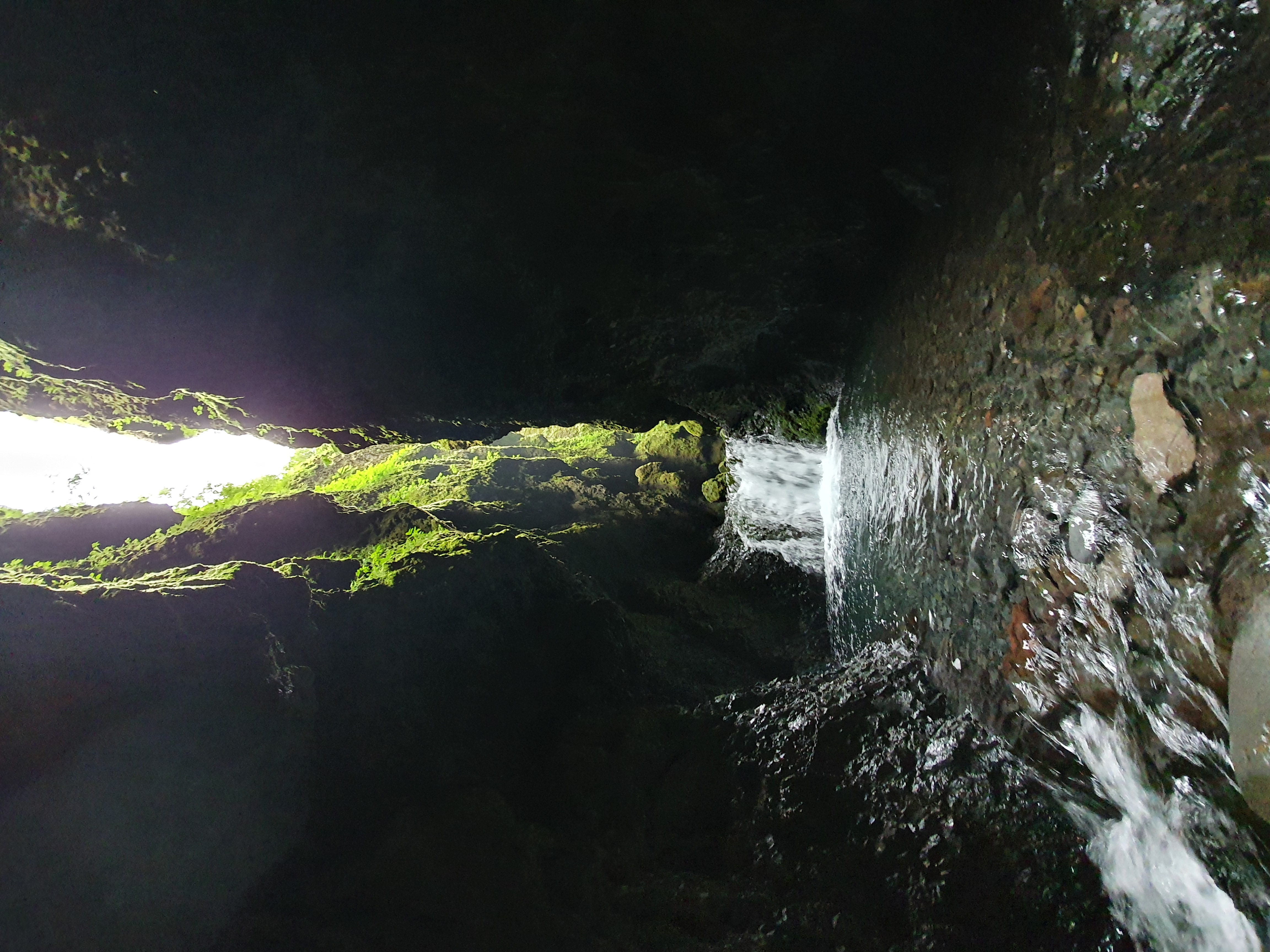 Waterfall visible through the narrow dark passage of Nauthúsagil with light streaming in