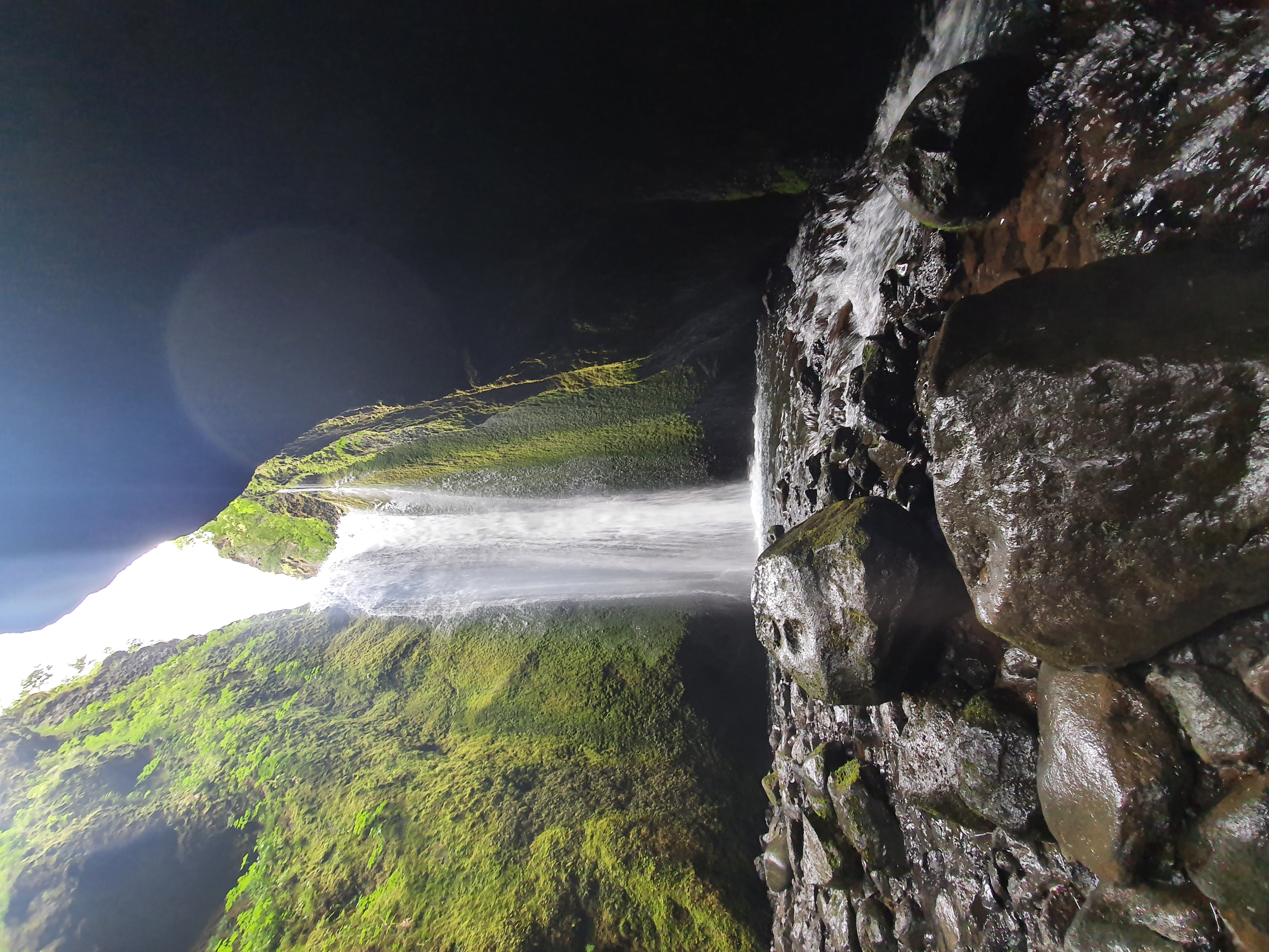 Looking up at the waterfall from below inside the dark Nauthúsagil canyon