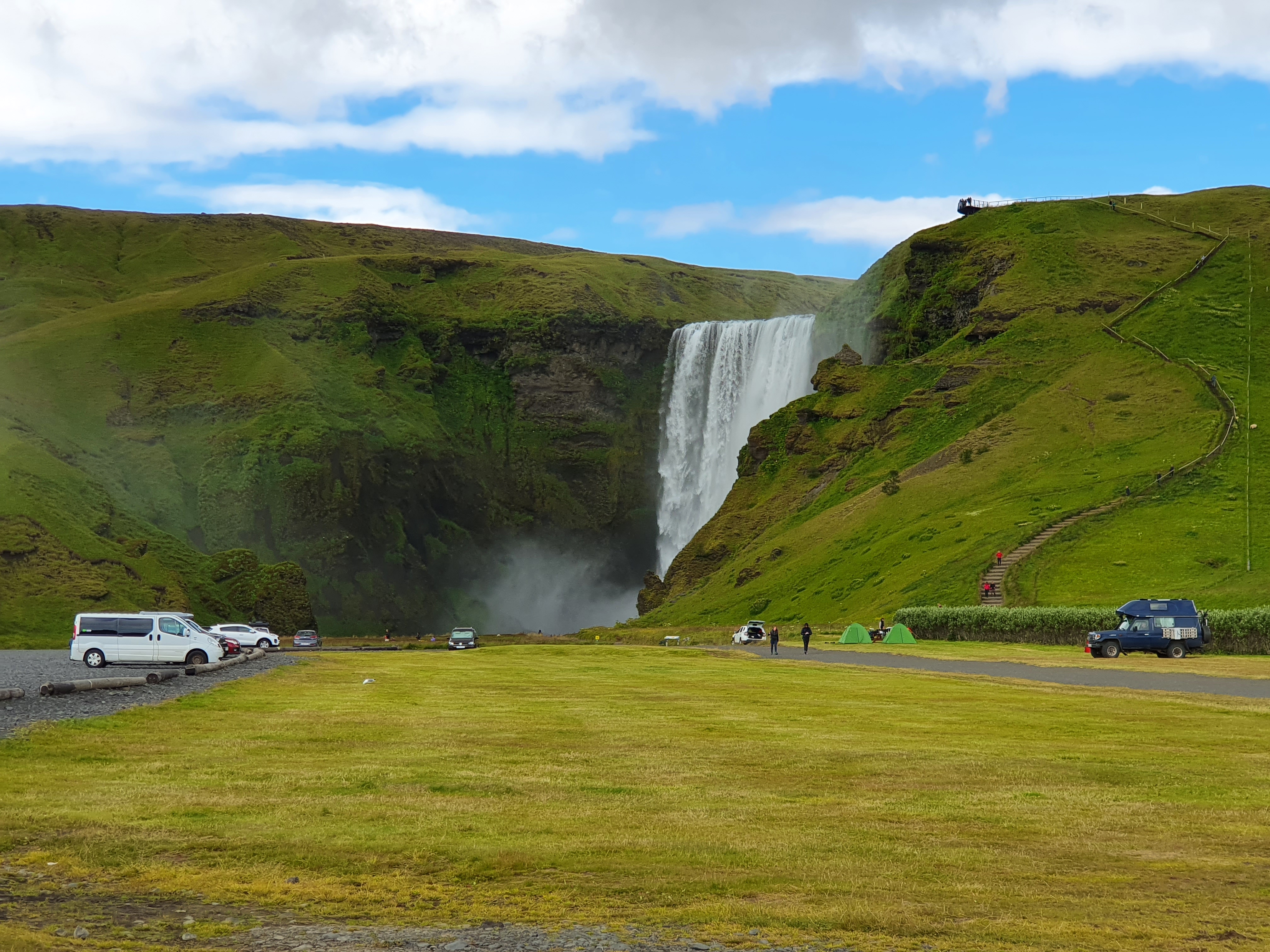 Skógafoss waterfall panoramic view with surrounding cliffs and green hillside